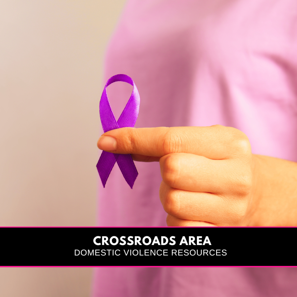 woman in a pink shirt holding a purple ribbon and a banner reading Crossroads Area Domestic Violence Resources